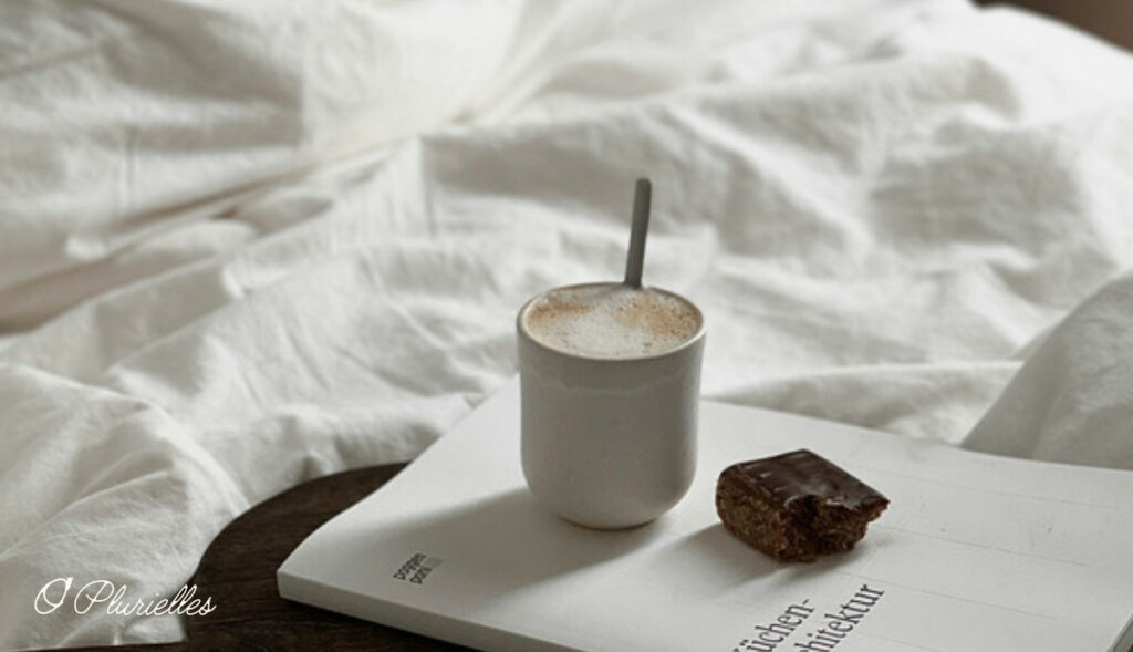 Tasse et carnet posés sur un lit blanc, pour rédiger sa page de soin